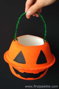 a hand holding an orange bucket with a jack o lantern on it