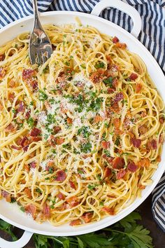 a plate of spaghetti with bacon and parmesan cheese on top, sitting on a striped table cloth