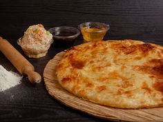 a pizza sitting on top of a wooden cutting board next to some spices and condiments