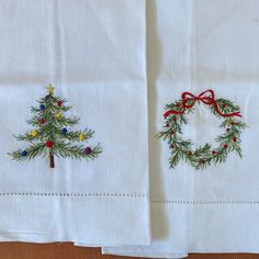 two embroidered christmas trees on white linens with red bows and green pine cones in the center