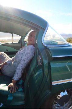 a woman sitting in the drivers seat of a green truck with her head out the window