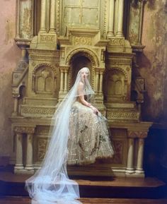 a woman in a wedding dress is sitting on a chair with a veil over her head