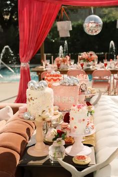 a table filled with cakes and desserts next to a swimming pool covered in red drapes