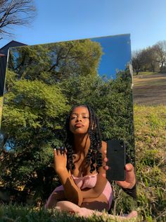 a woman sitting on the ground in front of a mirror holding up her cell phone