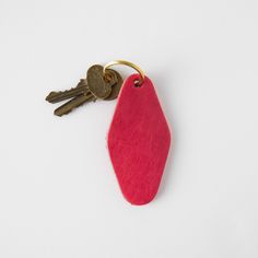 a red keychain with two keys hanging from it's side on a white surface