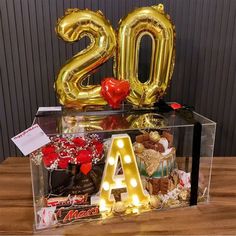 a clear box filled with balloons and letters that spell out the number twenty two in front of a wooden table