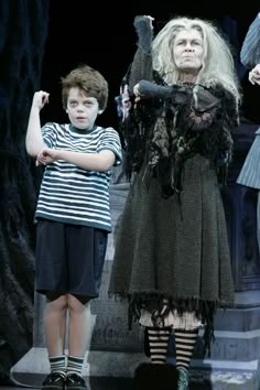 two children in costumes stand on stage with their hands up and one child holds his arm out