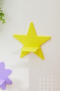 three different colored stars on a white wall next to a potted plant with green leaves