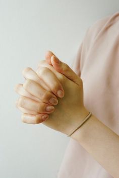 a woman is holding her hand up to the side while wearing a pink shirt and bracelet