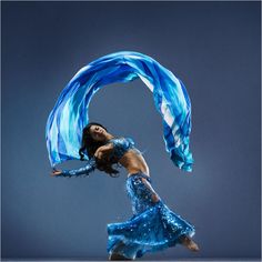 a woman in a blue dress is dancing with a scarf around her neck and legs