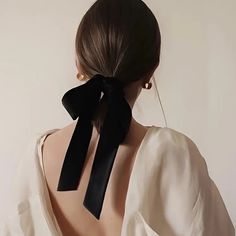 the back of a woman's head wearing a white blouse with a black bow