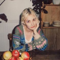 a woman sitting at a table with apples in front of her and looking to the side