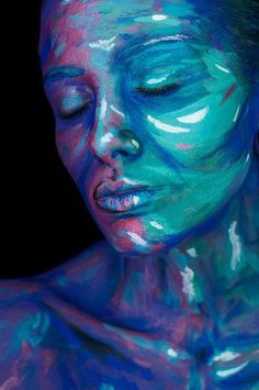 a woman covered in blue and green paint with her eyes closed to the side as if she is sleeping