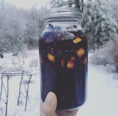 a hand holding a jar filled with liquid in the middle of a snow covered field