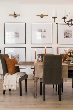 a dining room table and chairs with pictures on the wall behind them, along with candles