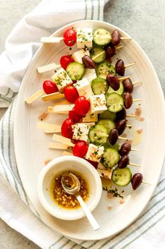 a white plate topped with cucumbers, tomatoes and olives on skewers