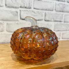 an orange glass pumpkin sitting on top of a wooden table next to a brick wall