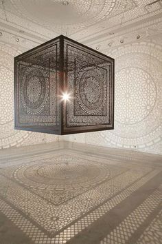 an intricately designed light fixture in the middle of a room with white walls and flooring