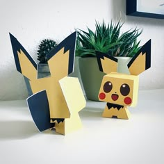 two paper pokemons sitting next to each other near a potted plant