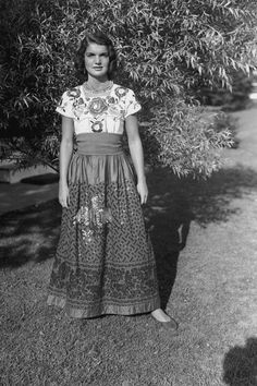 an old black and white photo of a woman standing in front of a tree with her hands on her hips