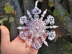 a hand is holding a snowflake made out of wire and paper, in front of a tree