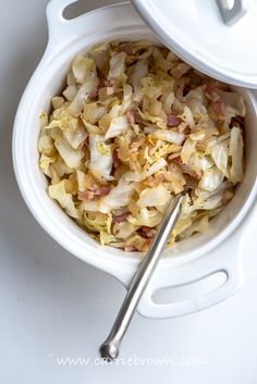 a white bowl filled with food next to a silver spoon on top of a table