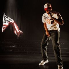 a man standing in front of an american flag on stage with his hand up to his mouth