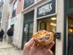 a person holding up a pastry in front of a store