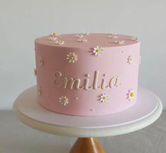 a pink cake decorated with daisies and the word'emila '