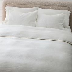 a bed with white sheets and pillows in a room