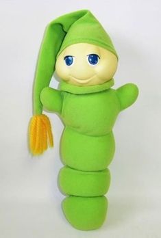 a green stuffed animal with a carrot in it's mouth and blue eyes, standing upright on a white background