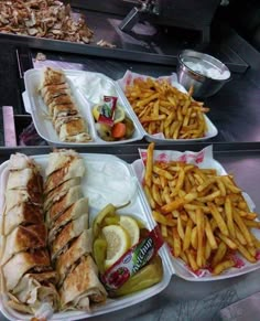 three trays filled with sandwiches and french fries on top of a table next to other foods