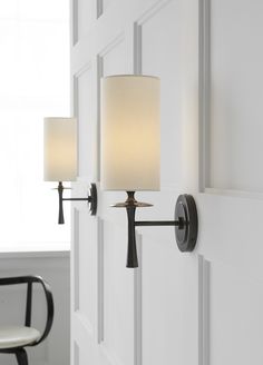 two lamps are on the wall in front of a door and chair next to it