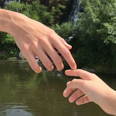 two people reaching out to touch each other in front of a river with waterfall behind them