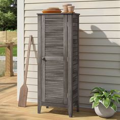 a tall wooden cabinet sitting on top of a wooden deck next to a house with a potted plant