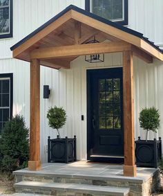 a black front door on a white house with two potted plants in the corner