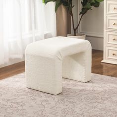 a white footstool sitting on top of a rug next to a potted plant