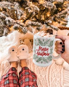 a woman holding a coffee mug with her feet up in front of a christmas tree