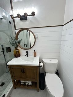 a white toilet sitting next to a wooden sink vanity in a bathroom under a round mirror