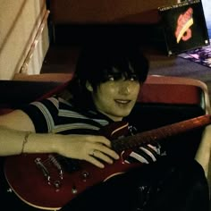 a young man sitting in a chair holding an electric guitar and looking at the camera