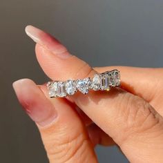 a woman's hand holding an engagement ring with five stones on it, and the band is in white gold