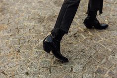 a woman in black boots and jeans standing on cobblestone