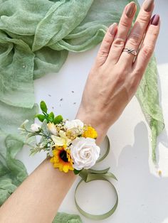 a woman's hand with a ring and flowers on her wrist next to a green scarf