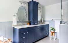 a bathroom with blue cabinets and two mirrors on the wall, along with white tile flooring