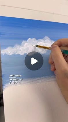 a person is painting an ocean scene with blue skies and white clouds in the background