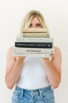 a woman is holding three books in her hands and covering her face with both hands