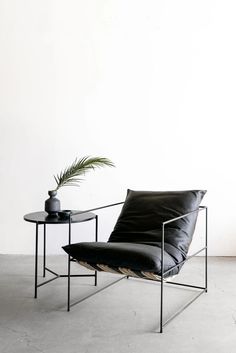 a black chair and table with a plant on it in front of a white wall