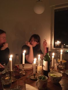 two people sitting at a table with candles in front of them and wine bottles on the table