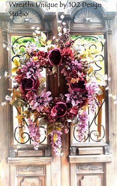 a wreath is hanging on the front door with purple flowers and greenery around it