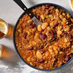 a bowl filled with chili and beans next to two glasses of beer on a table